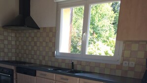 Ett kök med träskåp, kakel ovanför arbetsbänken, ett fönster med utsikt över grönområde och en diskmaskin.