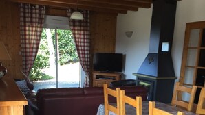 Ett mysigt rum med ett träpanelat tak, en soffa, en tv, en öppen spis och ett matbord med stolar.