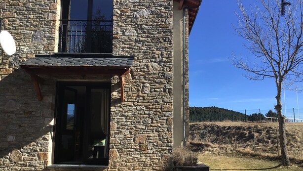 Ein Gebäude aus Stein mit Balkon, Tür und kleinem Garten.