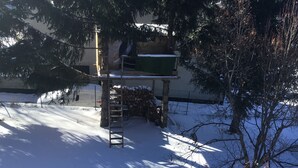 Schneebedecktes Freigelände mit einer Holzhütte, einer Leiter und einem Holzstapel.