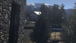 Ein Steinhäuschen mit Balkon, klarem Himmel und schneebedeckten Bergen im Hintergrund.