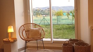 Una habitación con una silla de mimbre, un pequeño reposapiés y cestas de mimbre sobre una alfombra.