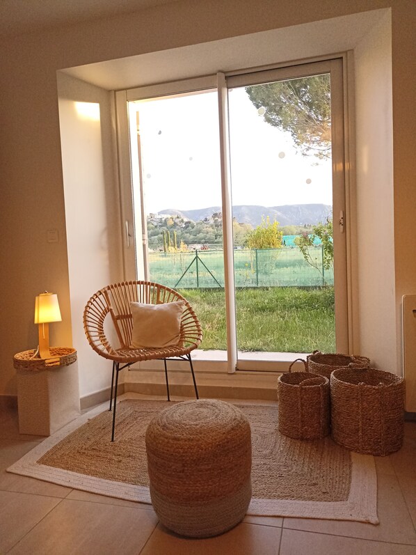 Una habitación con una silla de mimbre, un pequeño reposapiés y cestas de mimbre sobre una alfombra.