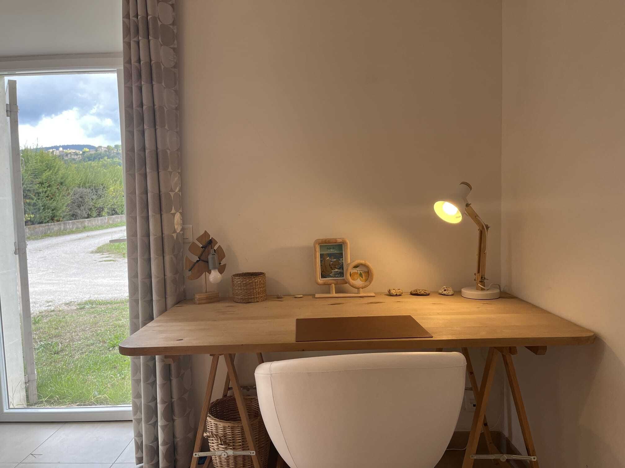 A wooden desk with a white chair, a desk lamp, a framed picture, and a small basket.