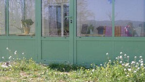 A green building with large windows, a potted plant, and a view of a landscape with trees and flowers. - PROMOTION summer: from 13/07 to 20/07 and 17/08 to 24/08 945 euros instead of 1500 eur (Verzeille)