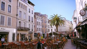 A bustling outdoor café area with tables and chairs, surrounded by buildings with balconies and storefronts. - Superb apartment ideally located in the city center with Clim (6 pers, 80m² ) (Nîmes)