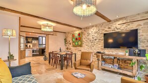 A living room with a sofa, armchair, coffee table, and a TV mounted on a stone wall. There is a dining area with a table and chairs in the background. - Superb apartment ideally located in the city center with Clim (6 pers, 80m² ) (Nîmes)