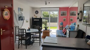 A room with a dining area, a sofa, a TV, and a sliding glass door leading to a balcony. - Newly built house, all mod cons (La Turballe)