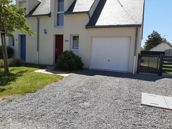 A two-story house with a white garage door, a red door, and a small garden area with a gravel driveway.