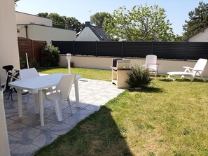 A patio area with a table and chairs, a barbecue grill, and a small garden.