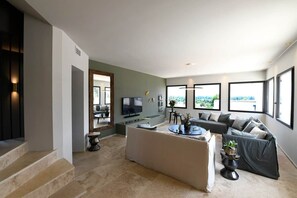 A modern living room with a sofa, TV, and large windows.
