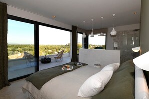 A modern bedroom with a large bed, a balcony with a view, and a shower area.