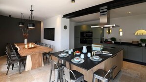 A modern kitchen with a central island, built-in appliances, and a dining area with a wooden table and chairs. - Les Loges en Provence - Villa "360 (Villeneuve-lès-Avignon)