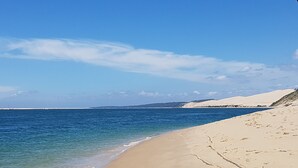 Een strand met helderblauw water, een zandstrand en duinen in de verte.