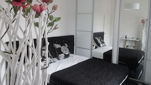 Een moderne slaapkamer met een groot bed, een spiegel en decoratieve witte takken met roze bloemen.