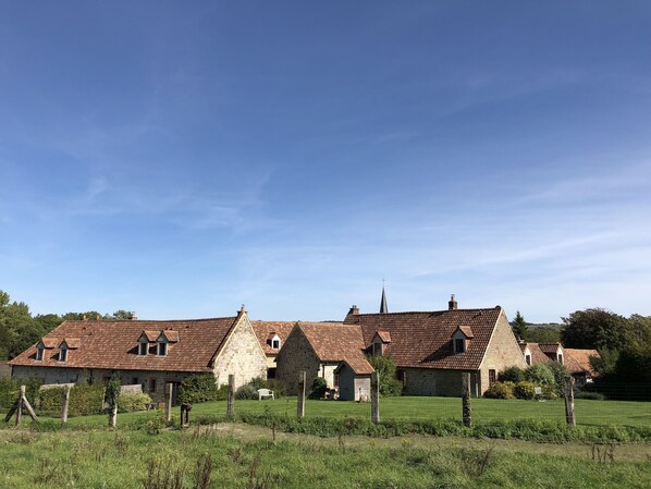 A row of traditional stone houses with red-tiled roofs, surrounded by a grassy field and a clear blue sky. - Gîte with covered swimming pool on the Opal Coast (Tingry)
