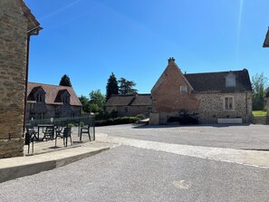 Un patio con edificios de piedra, un área cercada con bancos y un cielo azul despejado.