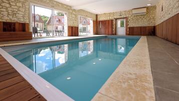 An indoor swimming pool with stone walls and wooden paneling, large windows, and a view of the outside.