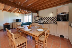 A wooden dining table with chairs, a television, and a kitchen with a microwave and oven. - Gîte with covered swimming pool on the Opal Coast (Tingry)