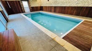 Una piscina interior rectangular con suelo de baldosas y paneles de madera alrededor.
