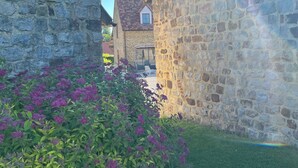 Un edificio de piedra con una ventana pequeña y un jardín lleno de flores moradas.