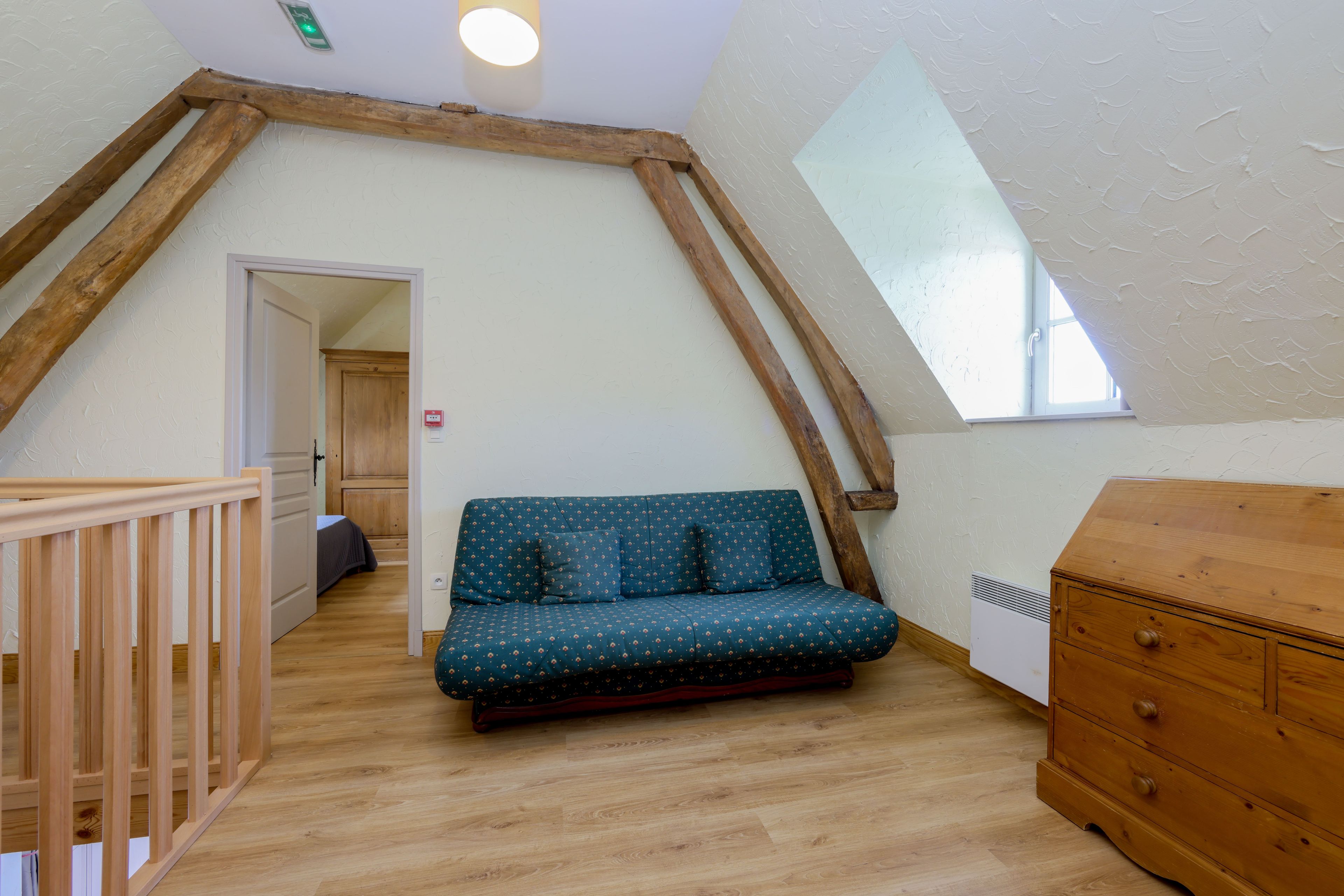 A loft bedroom with a wooden staircase, a sofa, a dresser, and a skylight.