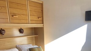 Ein ordentlich bezogenes Bett mit einer beigen Decke und zwei karierten Kissen, ein hölzernes Kopfteil und eine kleine Ablage mit Dekoration.