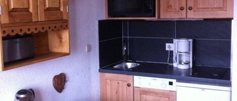 A compact kitchen with wooden cabinets, a microwave, a coffee maker, and a dishwasher.