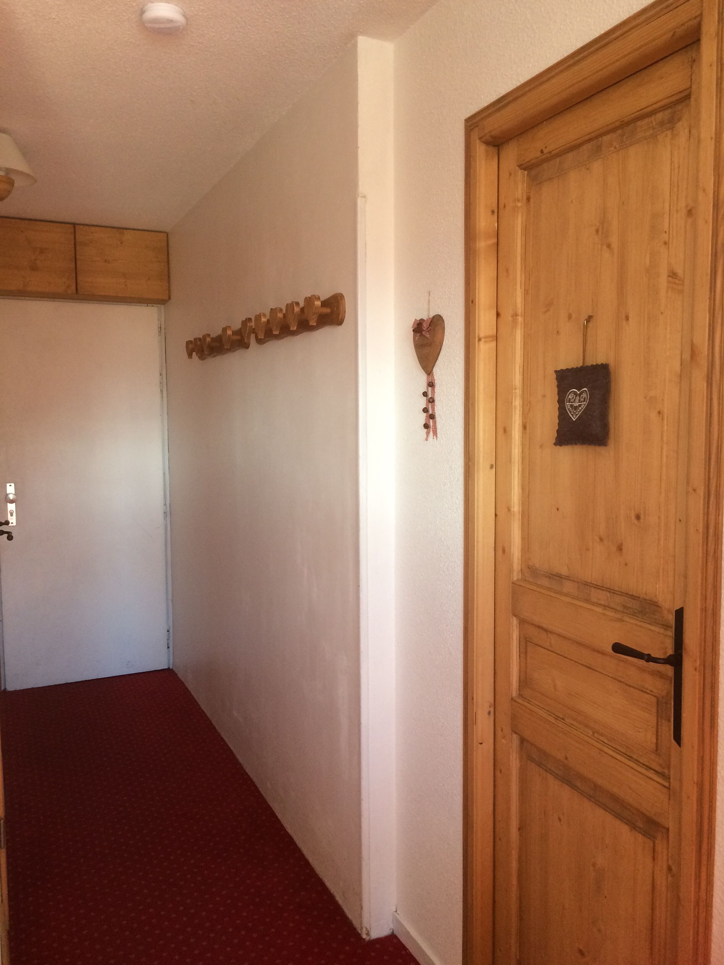 Un couloir avec une porte en bois, un décor mural en forme de cœur et une vis fixée au mur.