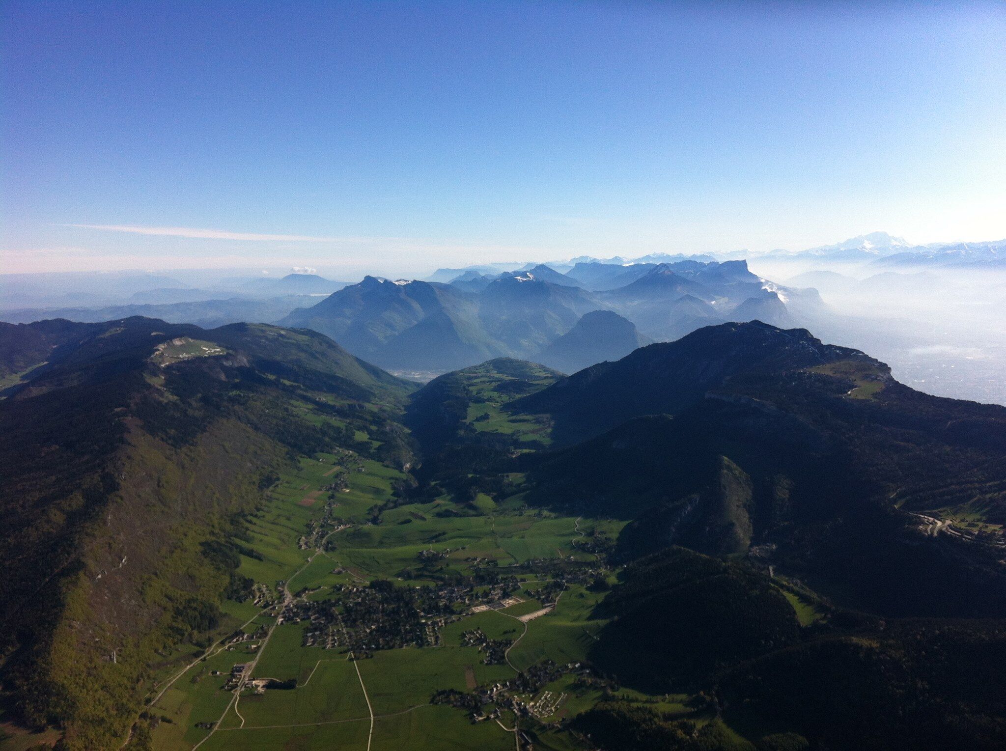 Un paysage montagneux, avec des vallées verdoyantes et, au loin, des sommets enneigés.