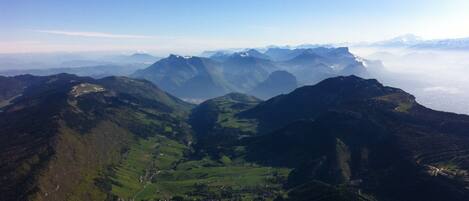 Un paysage montagneux, avec des vallées verdoyantes et, au loin, des sommets enneigés.