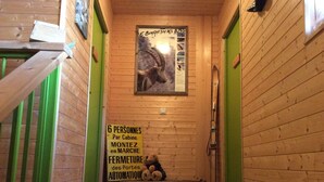 Un pasillo estrecho con paredes de madera y detalles verdes, un cartel en la pared, y un trineo con un osito de peluche.