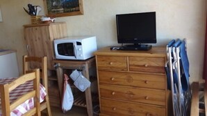 Pieni keittiö, jossa on mikroaaltouuni, televisio, puinen kaappi ja tuoli, jonka päällä on ruutukuviollinen pöytäliina.