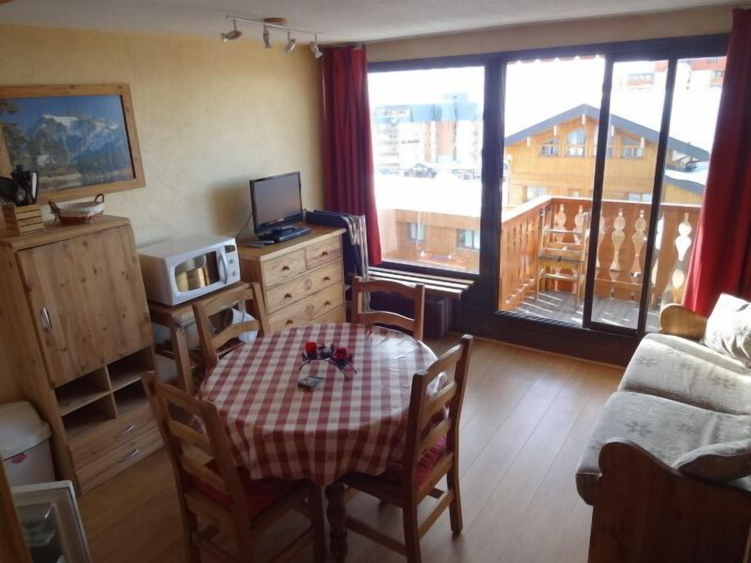 Ett rum med ett matbord, stolar, en soffa, en tv och ett fönster med utsikt över byggnader.