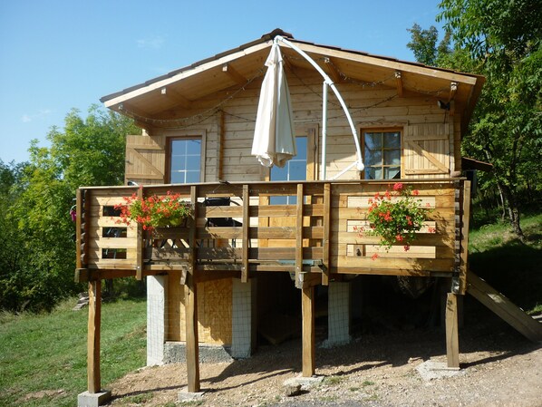 A wooden cabin with a balcony, a covered porch, and a small staircase leading up to the entrance. - WOODEN CHALET RENTAL IN THE HEART OF NATURE (Neschers)