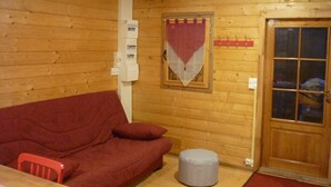Puinen sisustus, jossa on punainen sohva, pieni jalkarahi, ikkunalla varustettu ovi ja seinälle asennettu sähkökeskus.
