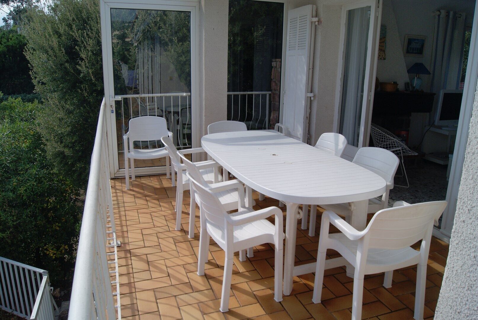 A balcony with a white table and chairs, a glass door, and a view of greenery.