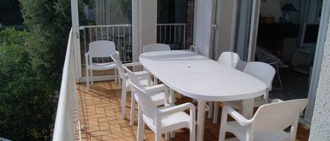 A balcony with a white table and chairs, a glass door, and a view of greenery.