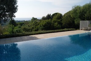 A clear blue pool with a tiled deck, surrounded by lush greenery and trees. - NEO-PROVENCAL VILLA WITH SECURE INFINITY POOL (Roquebrune-Sur-Argens)