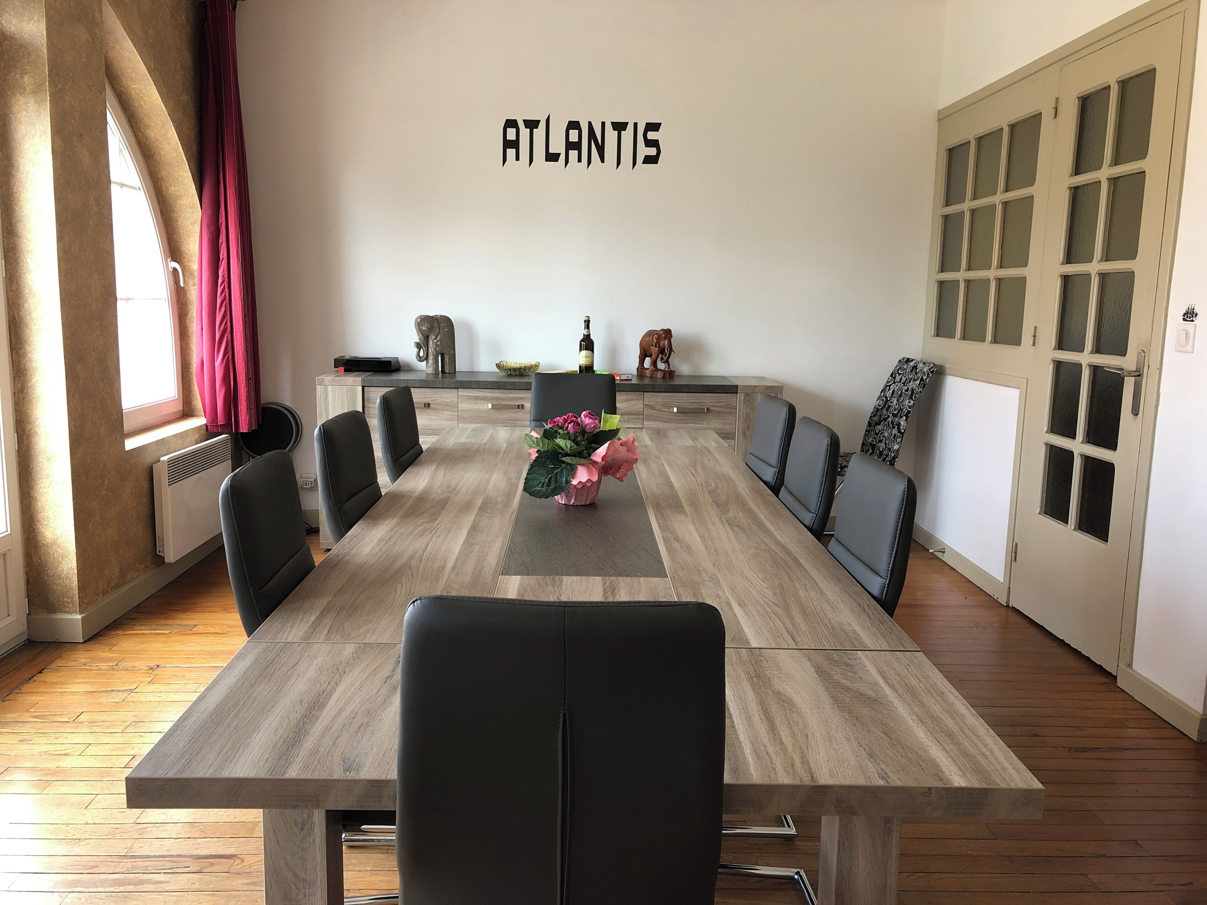 A dining area with a long table, chairs, a decorative centerpiece, and a wall-mounted sign reading 'ATLANTIS'.