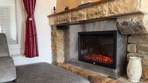 Ein Kamin aus Stein mit einem Fernsehbildschirm, ein graues Sofa und eine dekorative Vase.