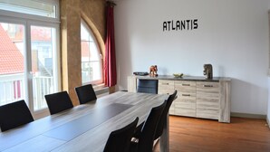 Ein moderner Essbereich mit einem langen Holztisch, schwarzen Stühlen, einer hellen Holzkommode und einem an der Wand befestigten Schild mit der Aufschrift 'ATLANTIS'.