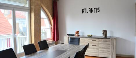 Un comedor moderno con una mesa larga, sillas negras, un mueble de madera con cajones y un cartel en la pared que dice 'ATLANTIS'.