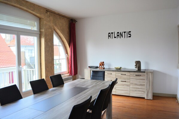 Un comedor moderno con una mesa larga, sillas negras, un mueble de madera con cajones y un cartel en la pared que dice 'ATLANTIS'.
