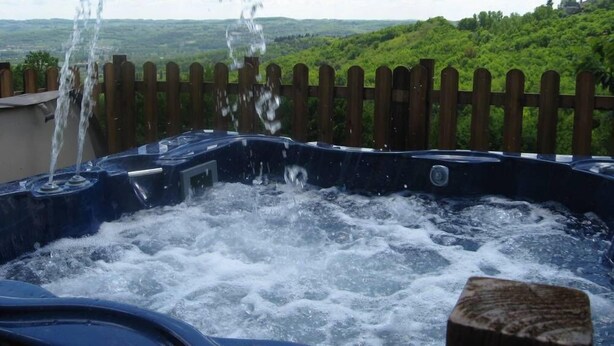 Un jacuzzi con chorros de agua, rodeado por una valla de madera y un exuberante paisaje verde al fondo.