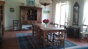 Une salle à manger avec une table et des chaises en bois, un lustre et un grand meuble avec des étagères.