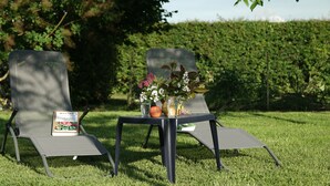 Deux chaises placées à l’extérieur, avec une table entre elles, un livre, un vase de fleurs et une bouteille.