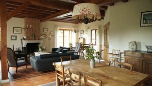 Un salon spacieux avec une cheminée, un coin repas avec une table et des chaises en bois, et un coin salon confortable avec un canapé et des fauteuils.