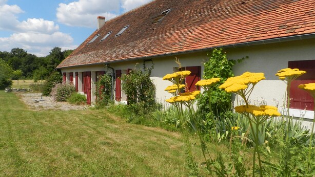 Un bâtiment blanc avec des volets rouges et un toit recouvert de tuiles rouges.
