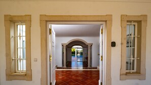 Un pasillo con suelo de baldosas, paredes blancas y una puerta que conduce a otra habitación.